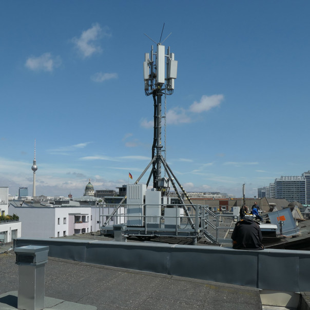 Mobilfunkmast ragt in den blauen Himmel über den Dächern von Berlin.