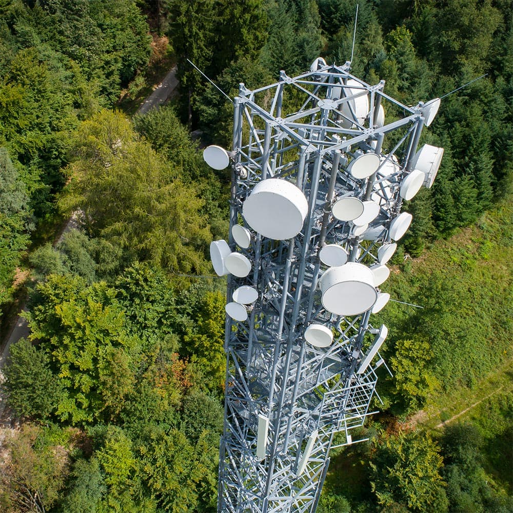 Bird's eye view of a transmission tower in front of a forest. New transmission towers are being built for the 5G network. However, the proximity to them and the electromagnetic fields is not dangerous.