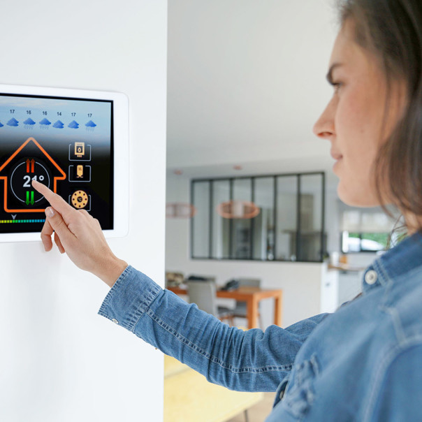 Eine Frau in Jeanshemd bedient ein Smart Home System auf dem Tablet an der Wand. Das neue 5G-Netz birgt neun Vorteile für unseren Alltag.