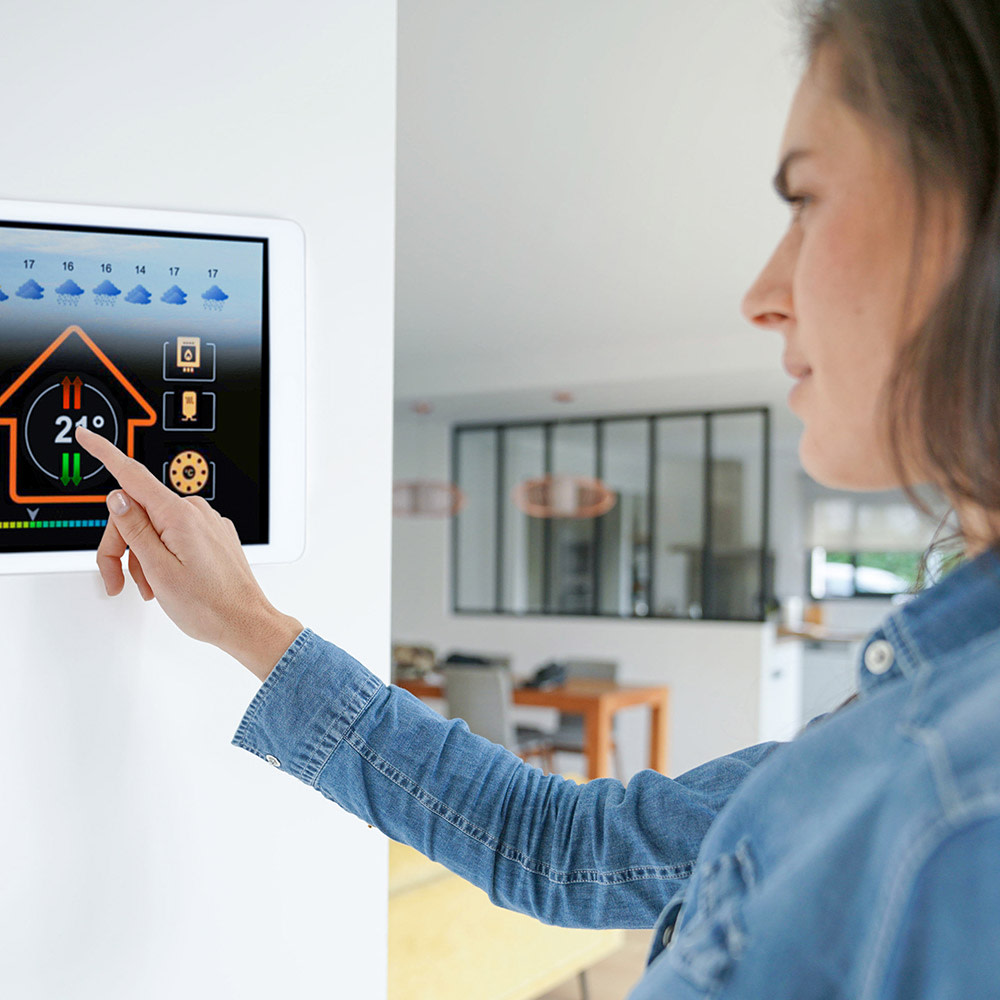 A woman in a denim shirt is using a smart home system on a tablet on the wall. The new 5G network has nine benefits for our everyday lives.