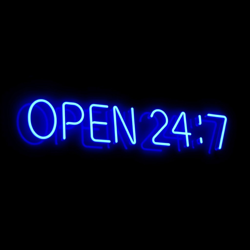 "'OPEN 24/7' in bright neon blue letters, glowing against a dark backdrop"