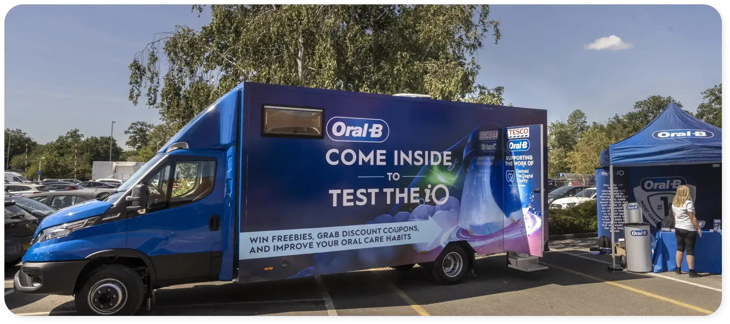 Woman holding an Oral-B iO electric toothbrush beside the Oral-B iO Experience bus