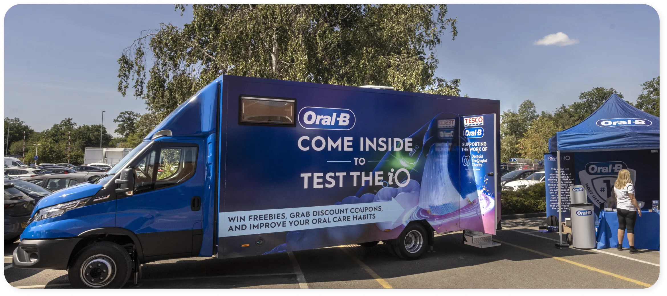 Woman holding an Oral-B iO electric toothbrush beside the Oral-B iO Experience bus 