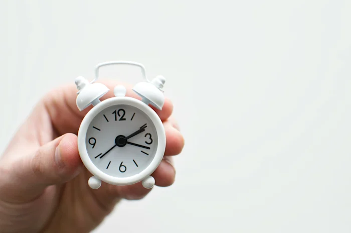 A hand holding a small white alarm clock