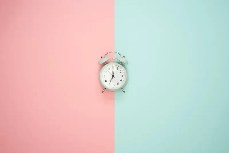 An alarm clock on a pink and teal background