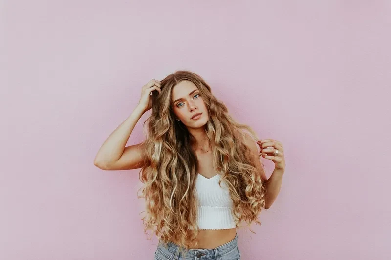 A woman wearing a white top and blue jeans on a pink background