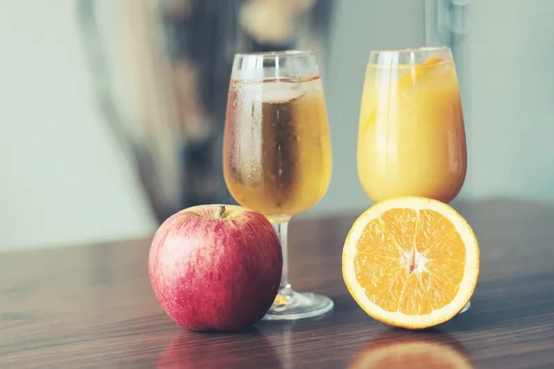 An apple, a glass of apple juice, an orange and a glass of orange juice.