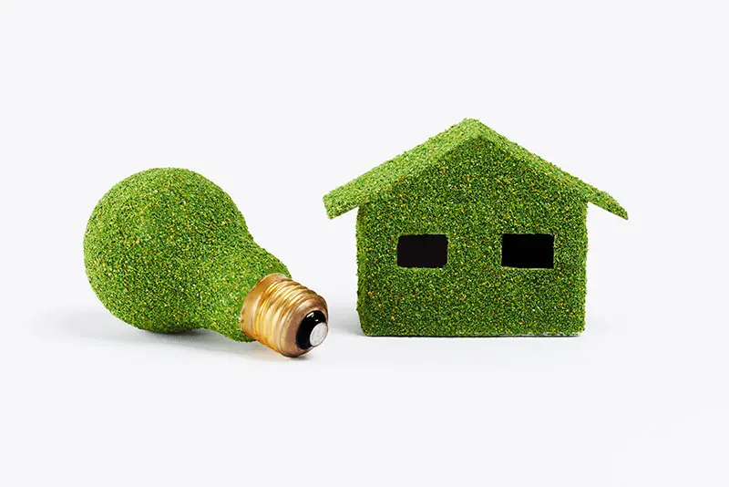 A grass covered light bulb and tiny house which demonstrate how being energy conscious can benefit everyone.