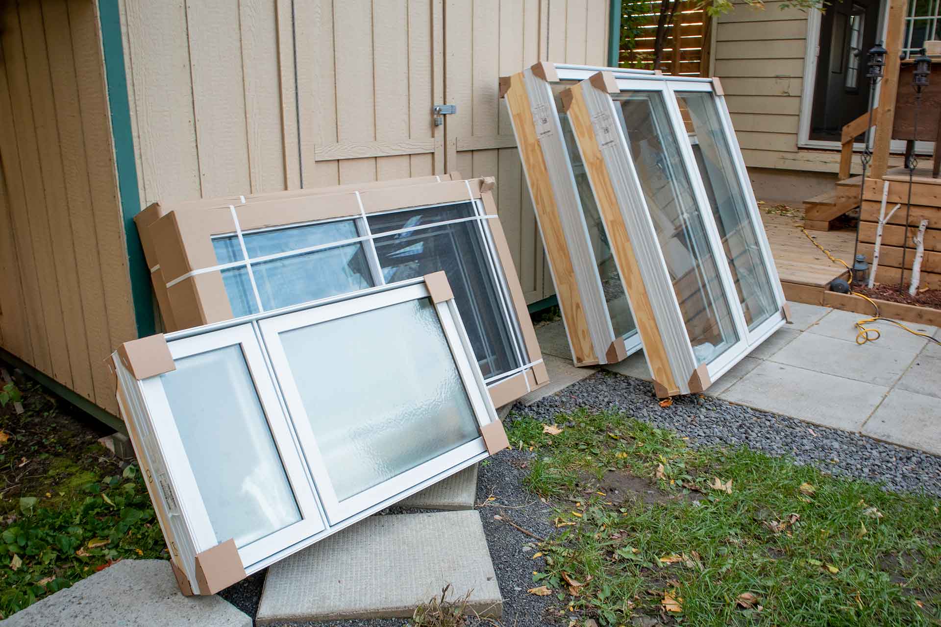 Replacement windows leaning up against a shed, awaiting installation.