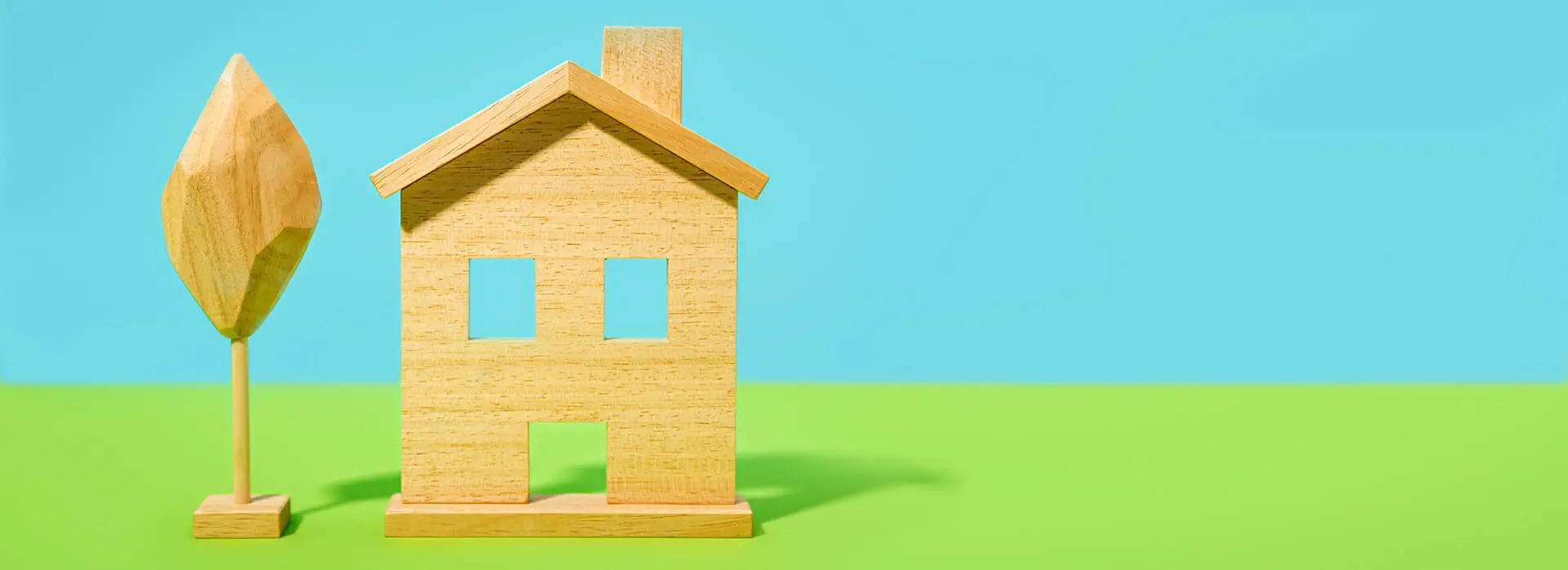 A wooden house with a wooden tree set on a blue and green pastel background.