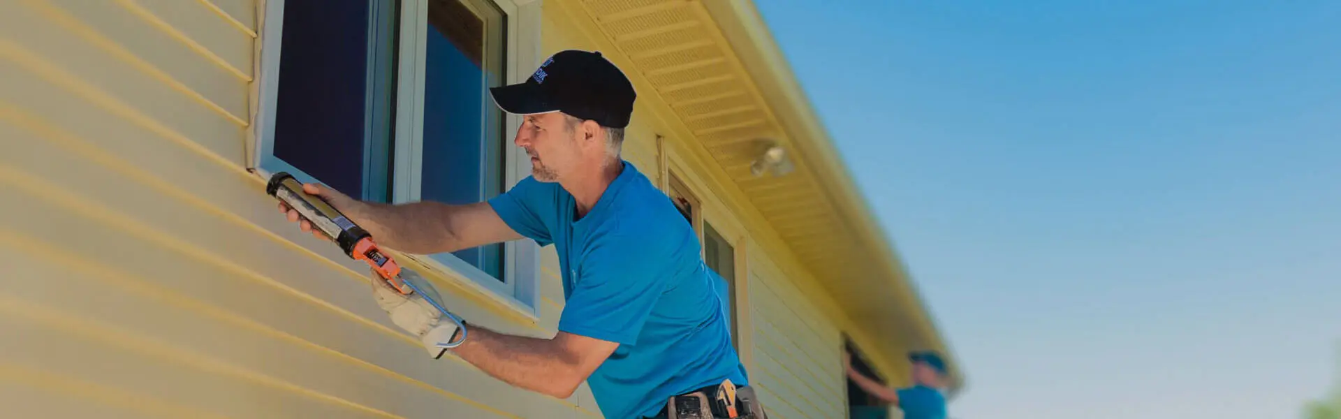 Two Nordik installers installing windows on house. One installer applying caulking to the new windows.