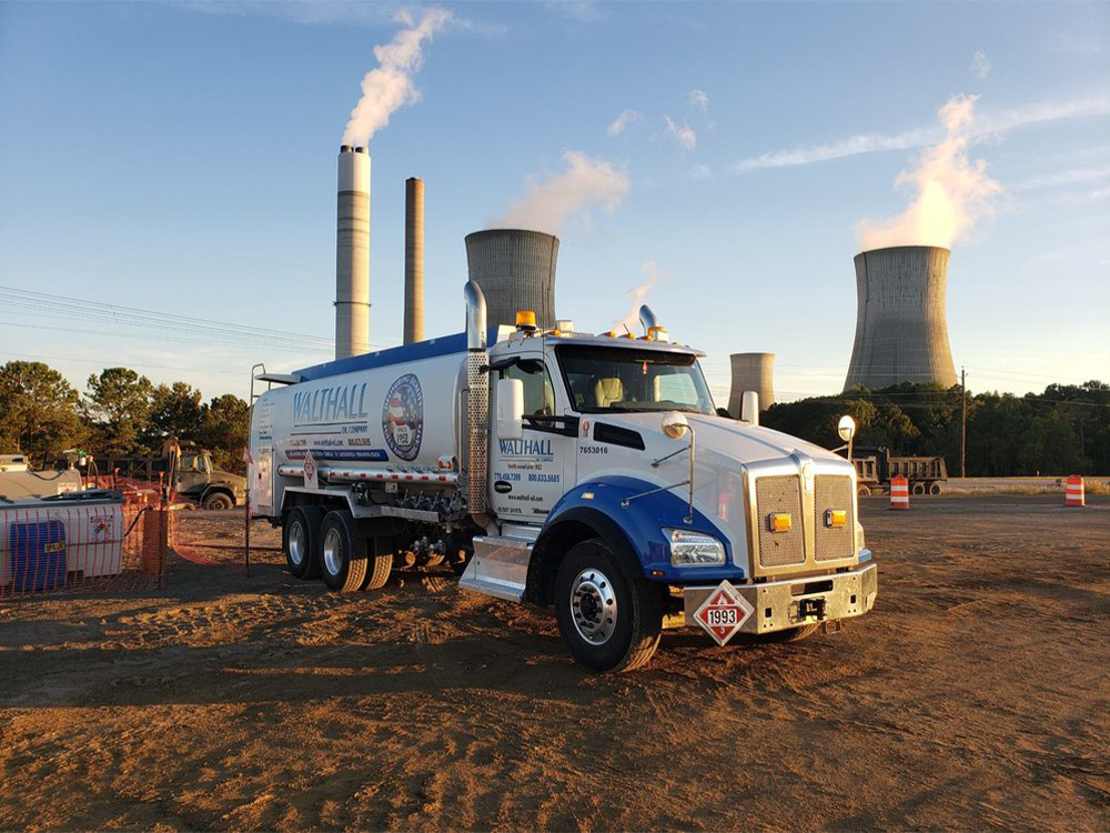 A Walthall Oil Company fuel tanker truck parked at an industrial site with smokestacks and cooling towers in the background.