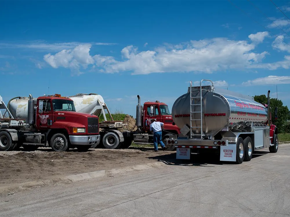 Sapp Bros. tanker trucks parked on a dirt lot under a blue sky, with a worker standing near one vehicle.