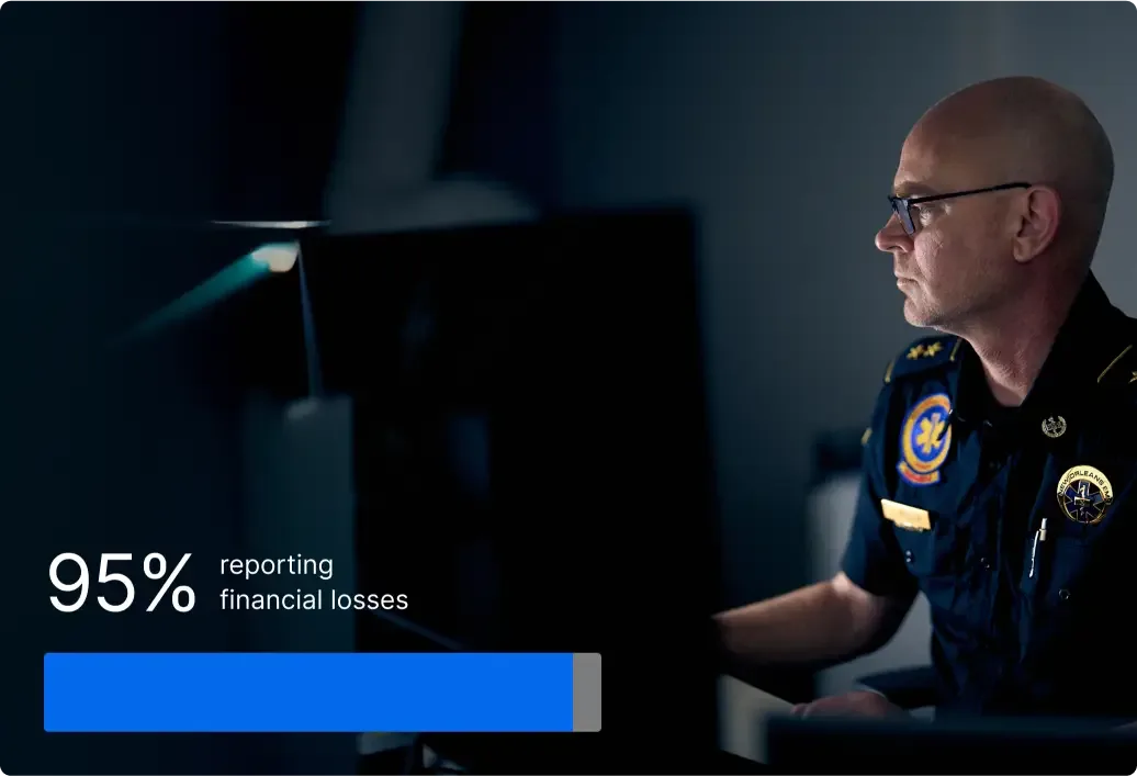 Police officer in uniform working at computer in dark room with statistic showing 95% reporting financial losses.