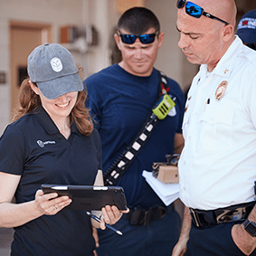 Three emergency responders in uniform reviewing information on a clipboard, wearing sunglasses and caps.