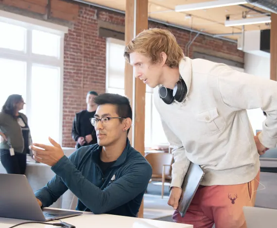 Two men looking at a laptop and discussing something.