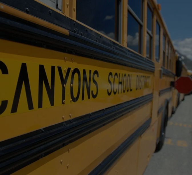Side view of a yellow school bus showing "CANYONS SCHOOL DISTRICT" text on its exterior against a blue sky.