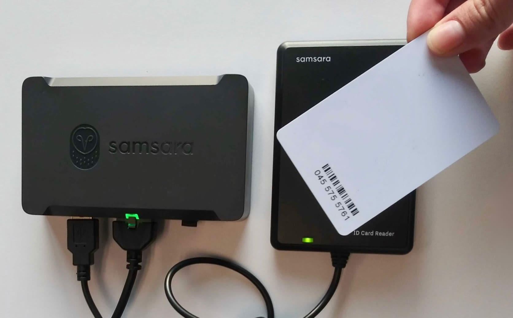 Samsara NFC hardware reader mocked up next to person holding smartphone connecting bluetooth device.