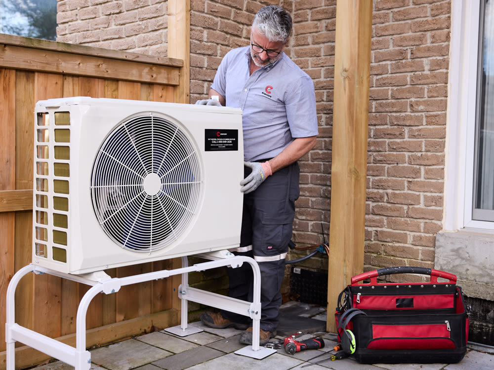 Employé d’Enercare inspectant un ventilateur extérieur avec un sac à outils rouge