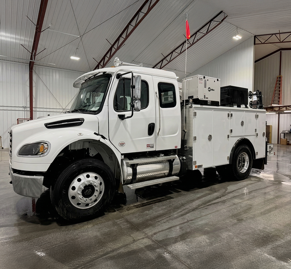White utility truck with extended cab and equipment compartments parked inside a metal warehouse building.