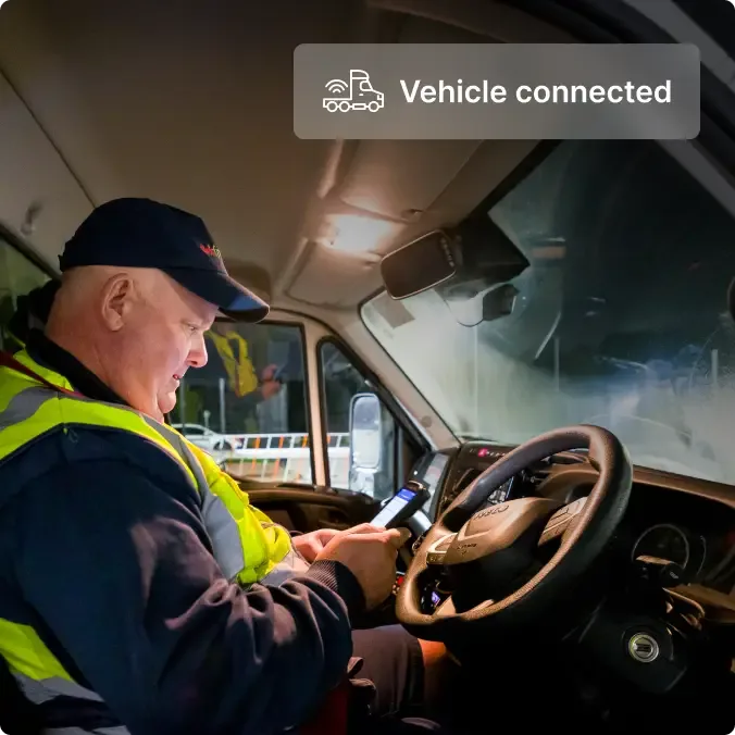 Driver in safety vest checking phone in truck cab with "Vehicle connected" notification displayed above.