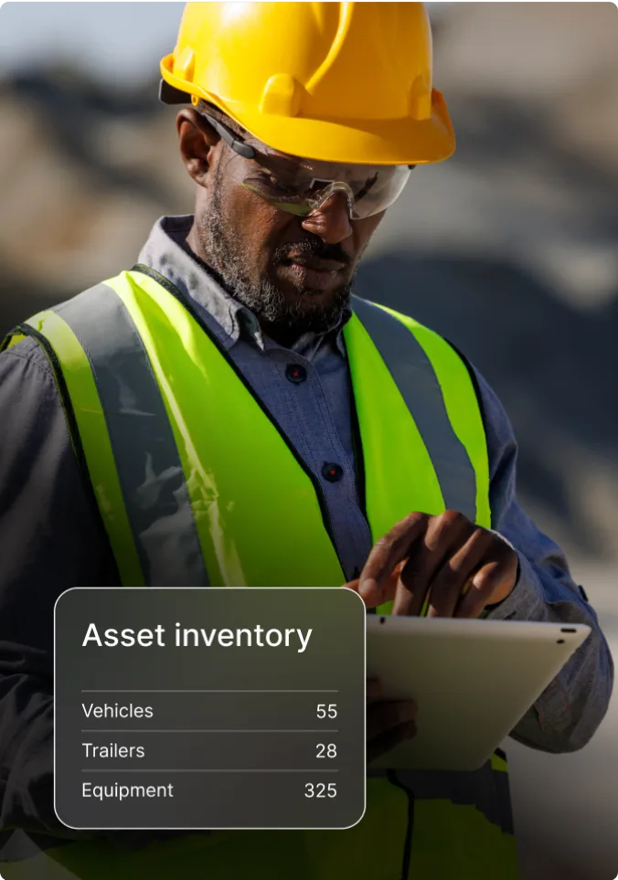 Construction worker in helmet and safety vest using tablet to check asset inventory of vehicles, trailers, and equipment.