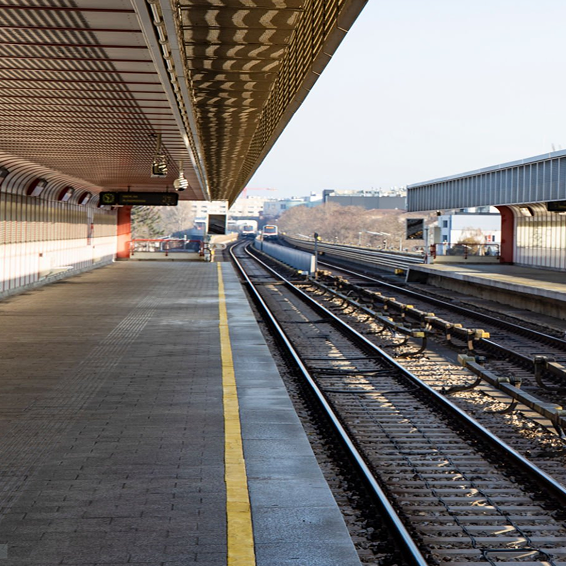 Empty train platform with covered waiting area, railway tracks extending into the distance, and yellow safety line.