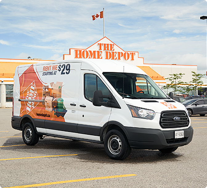 Fourgonnette de Home Depot avec une offre de location de 29 $ stationnée devant un magasin avec drapeau canadien sur le toit.