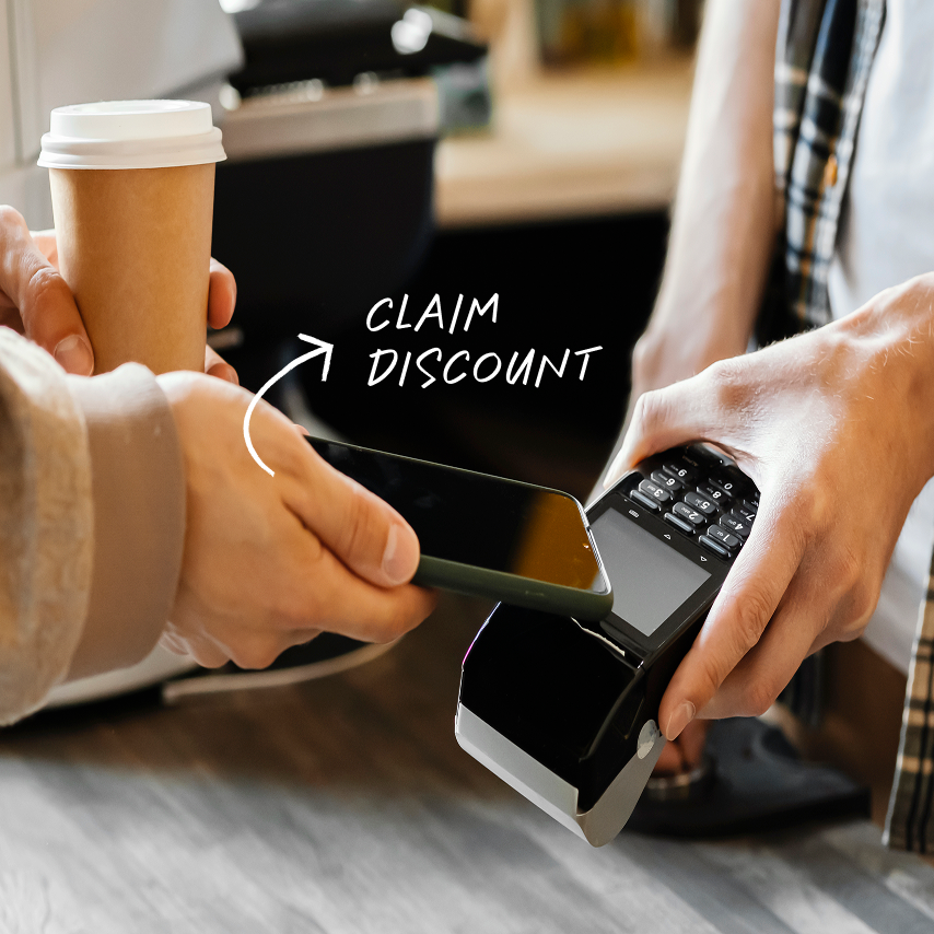 Person tapping phone on payment terminal to claim discount while holding a takeaway coffee cup.
