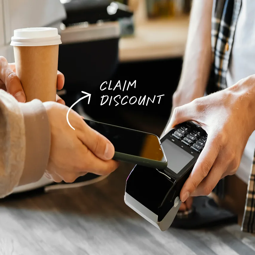 Person tapping phone on payment terminal to claim discount while holding a takeaway coffee cup.