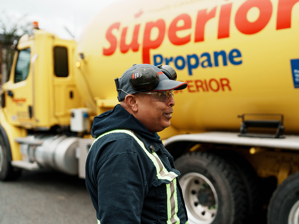 Employé en uniforme de sécurité souriant devant un camion-citerne jaune Superior Propane.