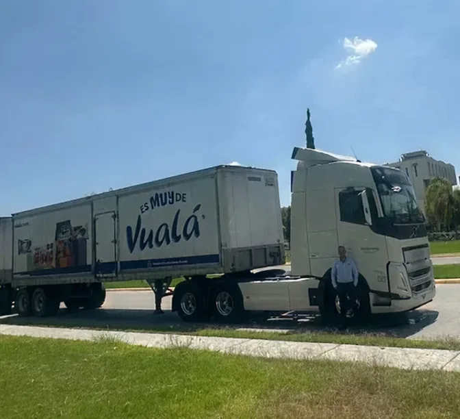 Camión blanco de transporte con remolque de la marca Vualá estacionado en una carretera bajo cielo azul despejado.