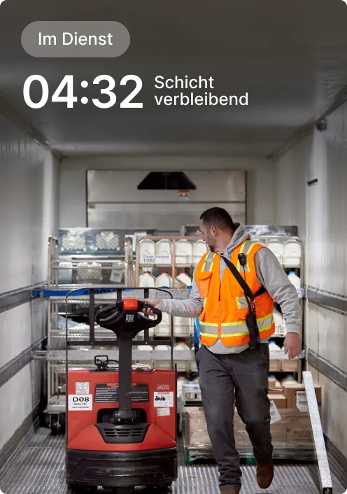 Arbeiter in orangefarbenen Sicherheitsweste bedient Hubwagen in Lieferwagen; Restschicht zeigt 4:32 an.