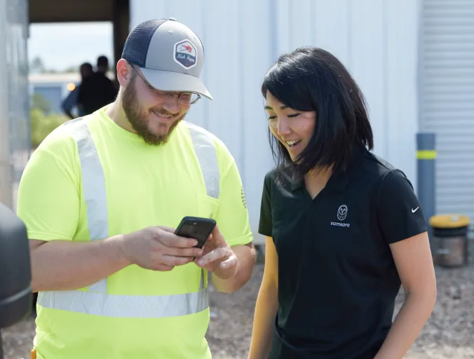 A Samsara employee explaining a dash cam to a worker as they stand outside of his truck.