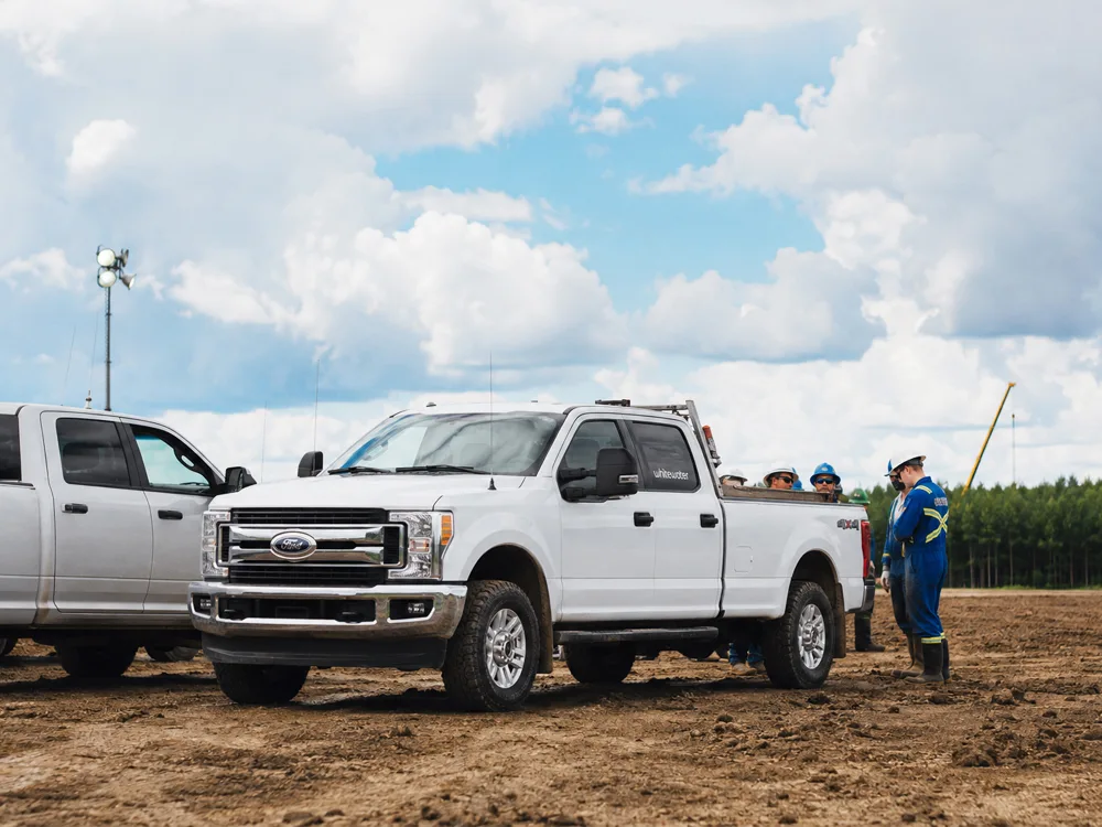 Two white Ford trucks in field with workers in blue uniforms and hard hats for Whitewater Management LP