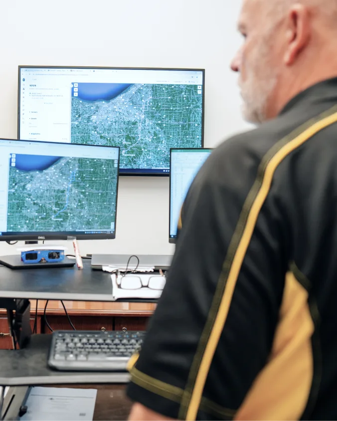 Fleet manager viewing aerial city maps and GPS tracking displays across multiple computer monitors