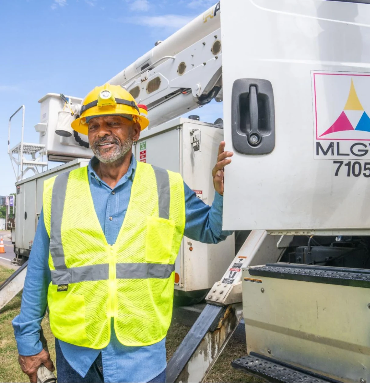 Driver in hard hat and safety vest smiling beside Memphis Light, Gas and Water service truck, MLG&W logo visible. 