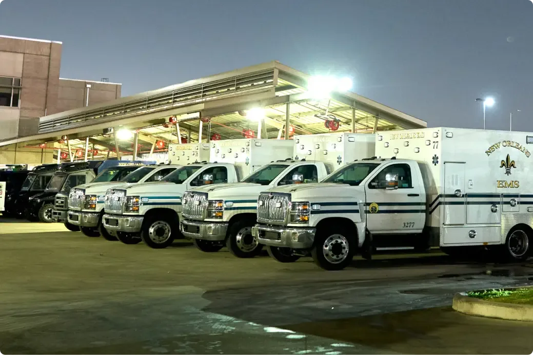 Row of New Orleans EMS ambulances parked at night under a lit station canopy.
