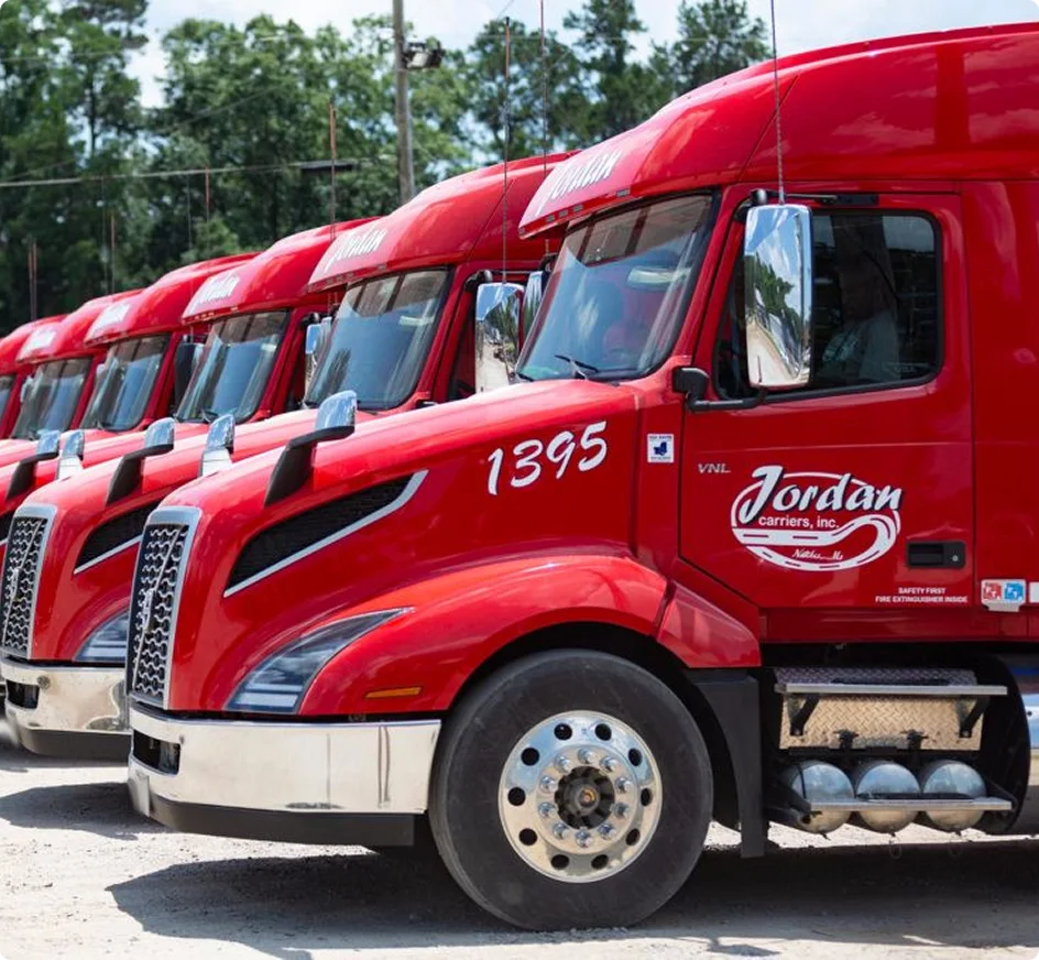 Row of bright red Jordan Carriers semi trucks lined up with truck number 1395 visible in the foreground.