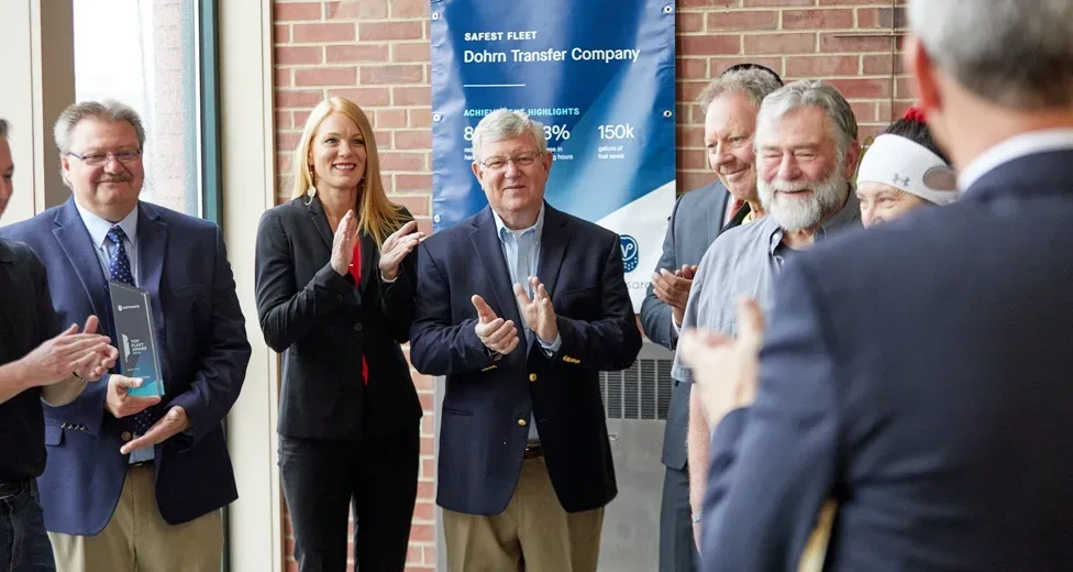 A group of people in business attire stands clapping