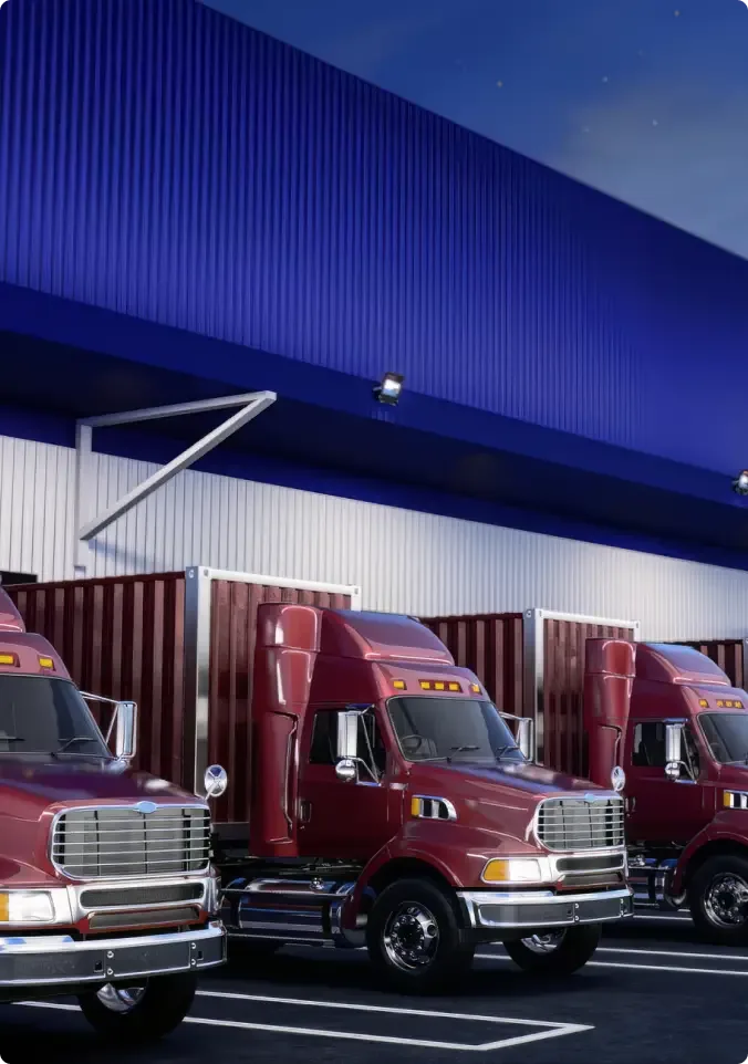 Three maroon semi trucks parked in a row at loading docks beneath a blue warehouse building at dusk.