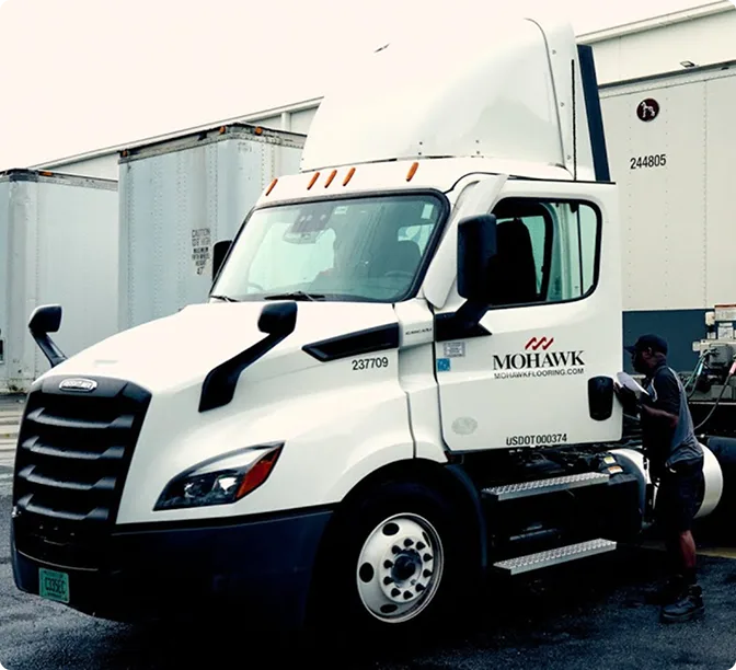 White Mohawk semi truck with driver entering cab, parked among other trailers in a shipping yard.
