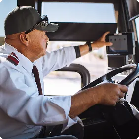 Buschauffeur in uniform en pet die het voertuig bestuurt, de bedieningselementen op het dashboard aanpast tijdens het sturen.