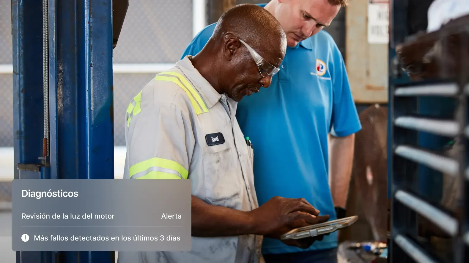 Dos mecánicos revisan diagnósticos del vehículo en una tableta, con alertas sobre incidencias de la luz del motor visibles.