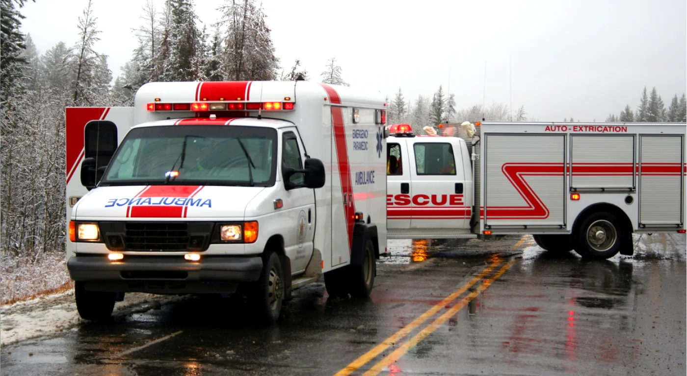 An ambulance and fire rescue truck with lights on, stopped on a road to help someone.