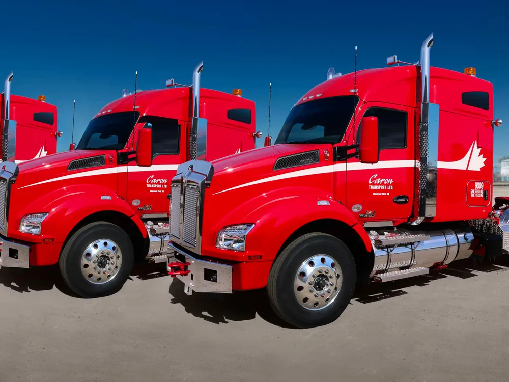 Row of bright red Caron Transport semi trucks with white accents parked side by side against a clear blue sky.