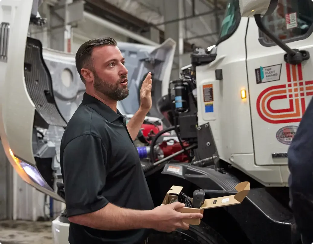 Technician holding a package next to industrial CNC machinery in a manufacturing facility.