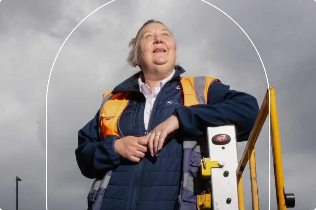 Hulpverlener met een felgeel New Orleans EMS-hesje, een zwarte pet en een zonnebril, staand bij voertuigen.