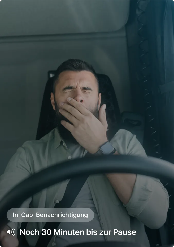 Person gähnt beim Fahren, mit In-Cab-Benachrichtigung, die am unteren Bildschirmrand „Noch 30 Minuten bis zur Pause“ anzeigt.