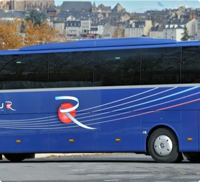 Blue tour bus with red and white logo parked in front of a European town with autumn trees and historic buildings.